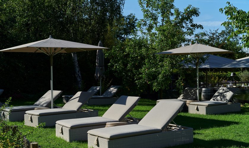 Sonnenliegen mit großen Sonnenschirmen stehen auf einer Wiese in einem grünen Garten als Teil eines Hotel Arrangements im Harz