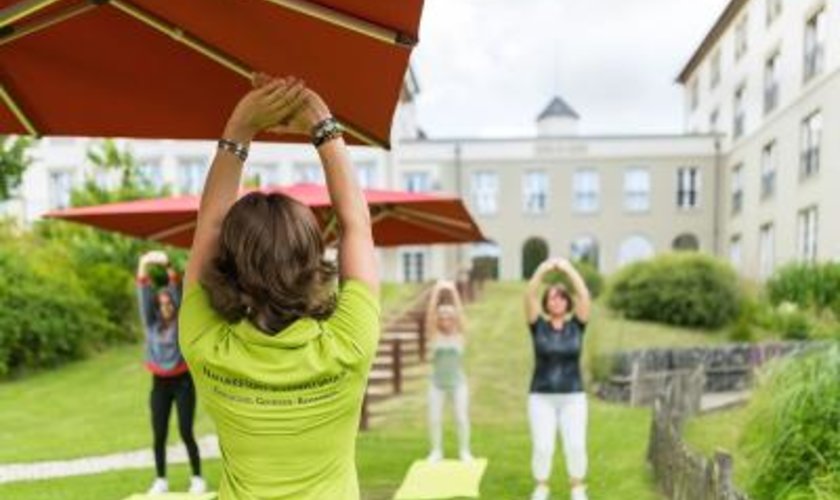 Hotelgäste machen unter Anleitung Yoga vor dem Hotel Hotelgäste machen unter Anleitung Yoga im Hotel mit Massagen im Harz