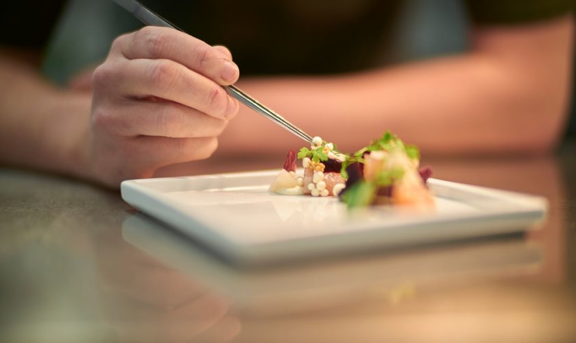 Eine Person dekoriert ein kunstvoll angerichtetes Gourmetgericht auf einem weißen Teller im Restaurant in Stolberg im Harz
