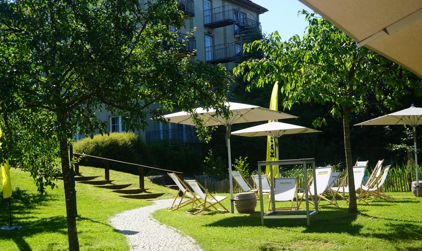 Auf dem Rasen im Hotelgarten stehen Sonnenschirme und Liegestühle für eine Veranstaltung mit dem Hotel im Hintergrund.