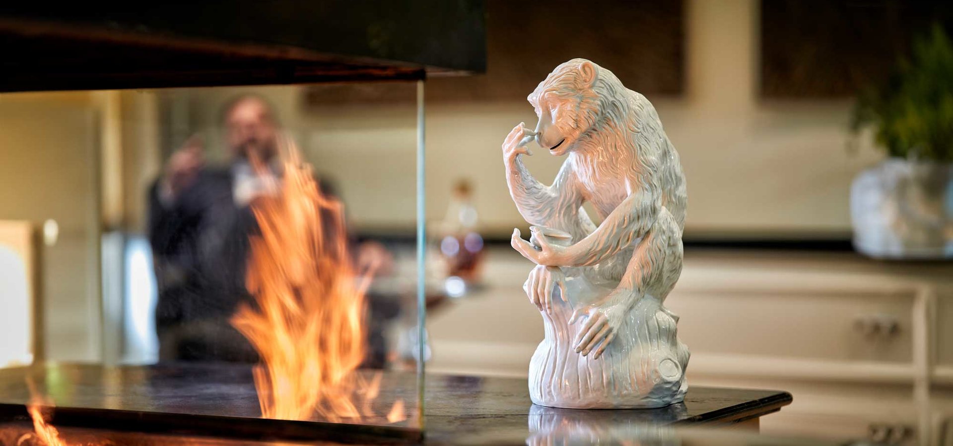 Detailreiche Affenfigur als Kunst im Hotel neben einem offenen Kaminfeuer