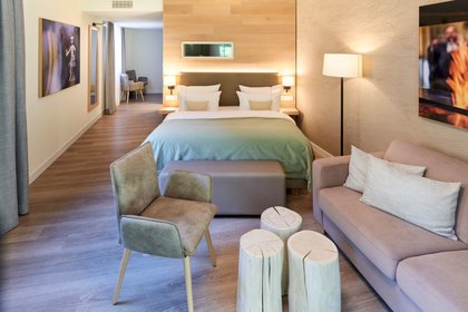 In einem modernen Hotelzimmer steht ein gemütliches Doppelbett mit indirekter Beleuchtung und warmen Wandtönen.