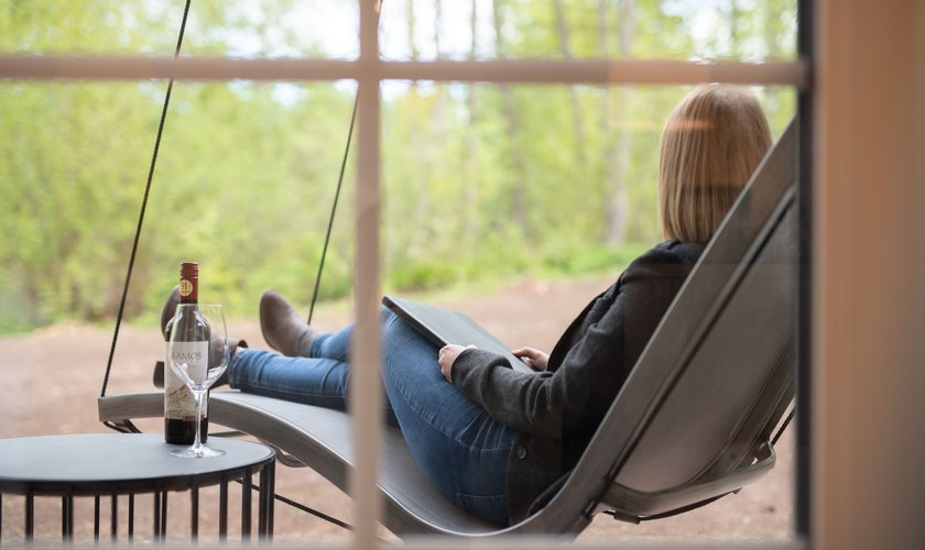 Eine Frau liegt in einer Hängematte vor dem Zimmer der Neuen Landresidenz auf der Terrasse mit einem Glas Wein neben sich stehend.
