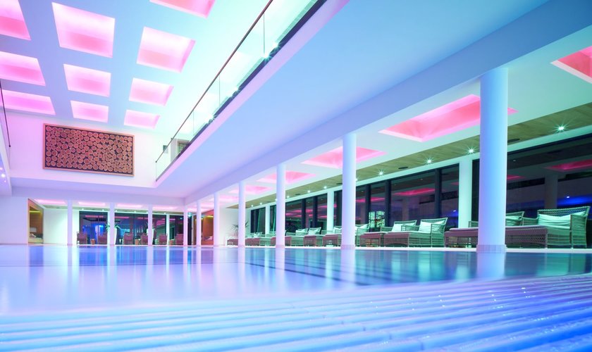 Modernes Hallenbad im Wellnesshotel im Harz mit farbiger Beleuchtung und Liegebereich, ideal für Entspannung und Erholung im stilvollen Ambiente