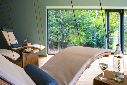 Im Ruheraum Wipfelnest hängen geschwungene Liegen von der Decke und durch die großen Fenster geht der Blick in den Wald.