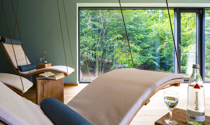 Im Ruheraum Wipfelnest hängen geschwungene Liegen von der Decke und durch die großen Fenster geht der Blick in den Wald.