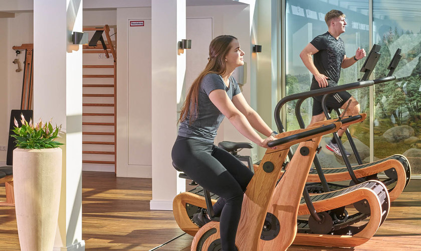 Heller Fitnessraum mit Holz-Trainingsgeräten und großen Glasfenstern im Wellnesshotel Harz