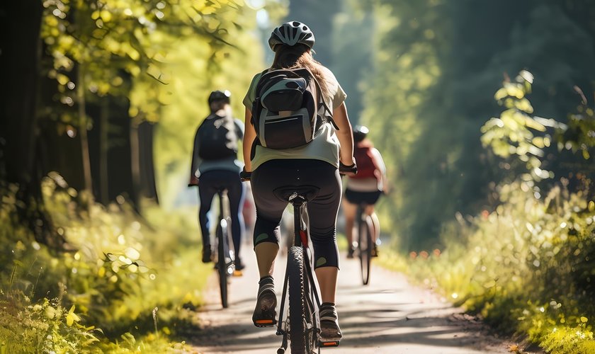 Gruppe von Radfahrern im Aktivurlaub fährt auf einem Waldweg durch sonnendurchflutete Bäume im Harz