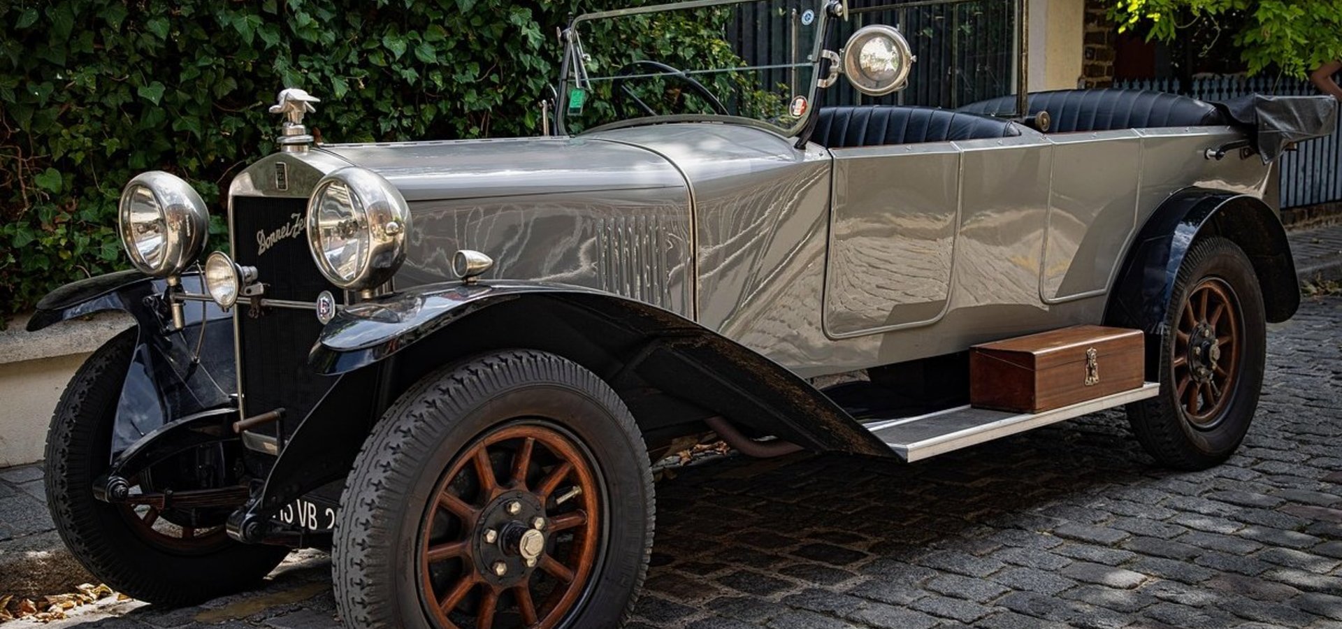 Ein eleganter Oldtimer Donnet Zedel in grau steht auf einer gepflasterten Straße mit Grün im Hintergrund.